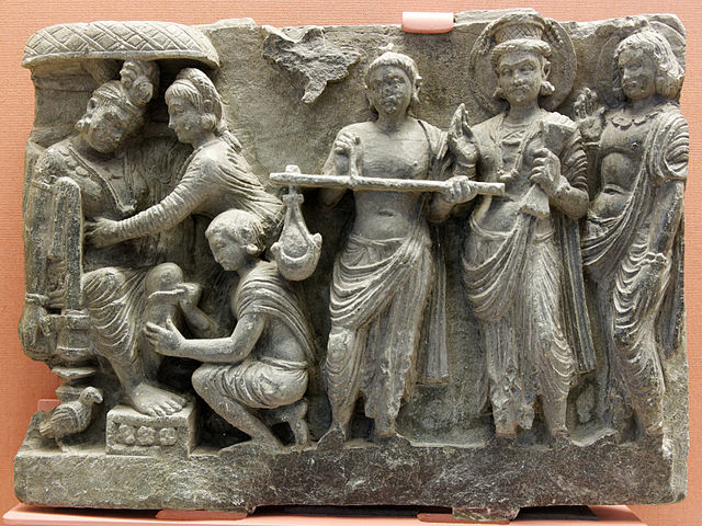King Shibi seated while an attendant cuts flesh from his thigh to outweigh a dove on the scales, Gandharan schist relief, 2nd-3rd century CE