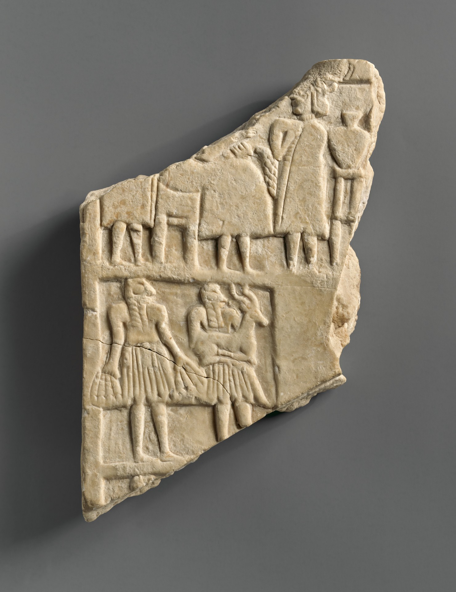 Fragmentary stone plaque with standing attendants above and seated banquet figures below.