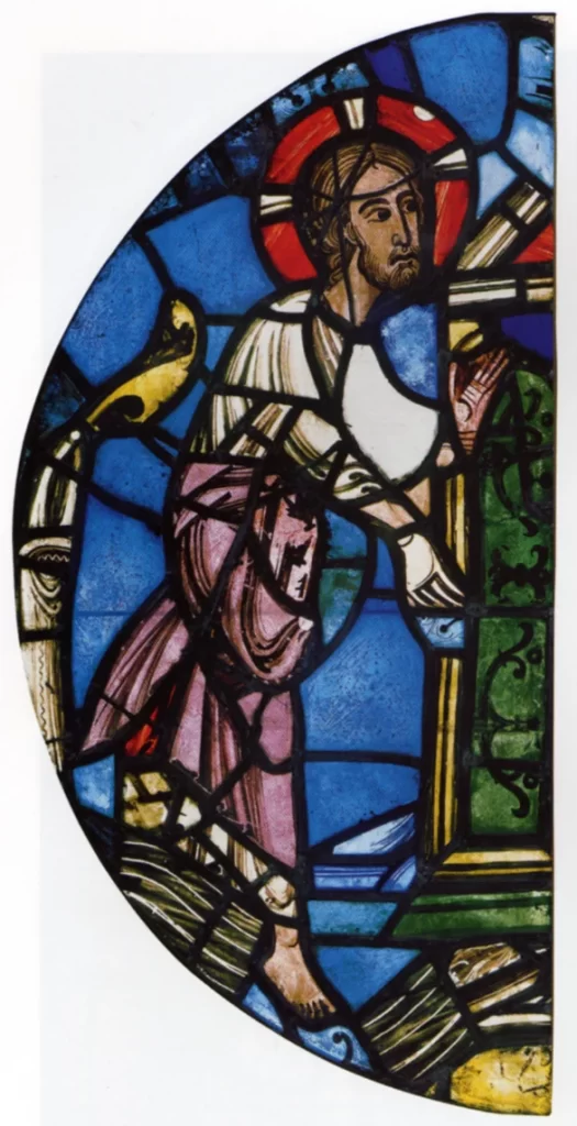 A half-round panel of medieval stained glass in deep blue: a bearded figure with a red halo, in white and rose robes, reaches out to the frame of a door.