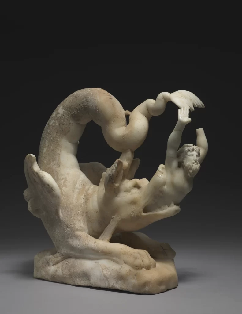 A small marble sculpture of a sea monster with a coiled tail spitting out a bearded man, who comes out head first with his arms raised.
