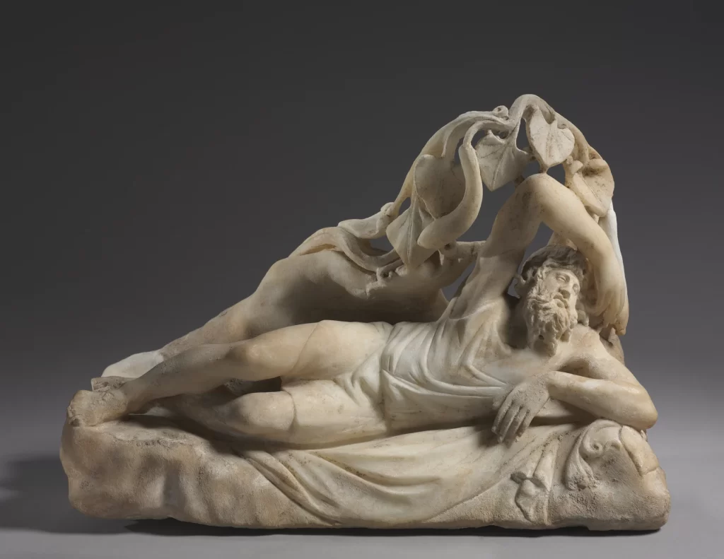 A marble sculpture of a bearded man lying at his ease on his side, one arm bent behind his head, under the broad leaves of a vine.