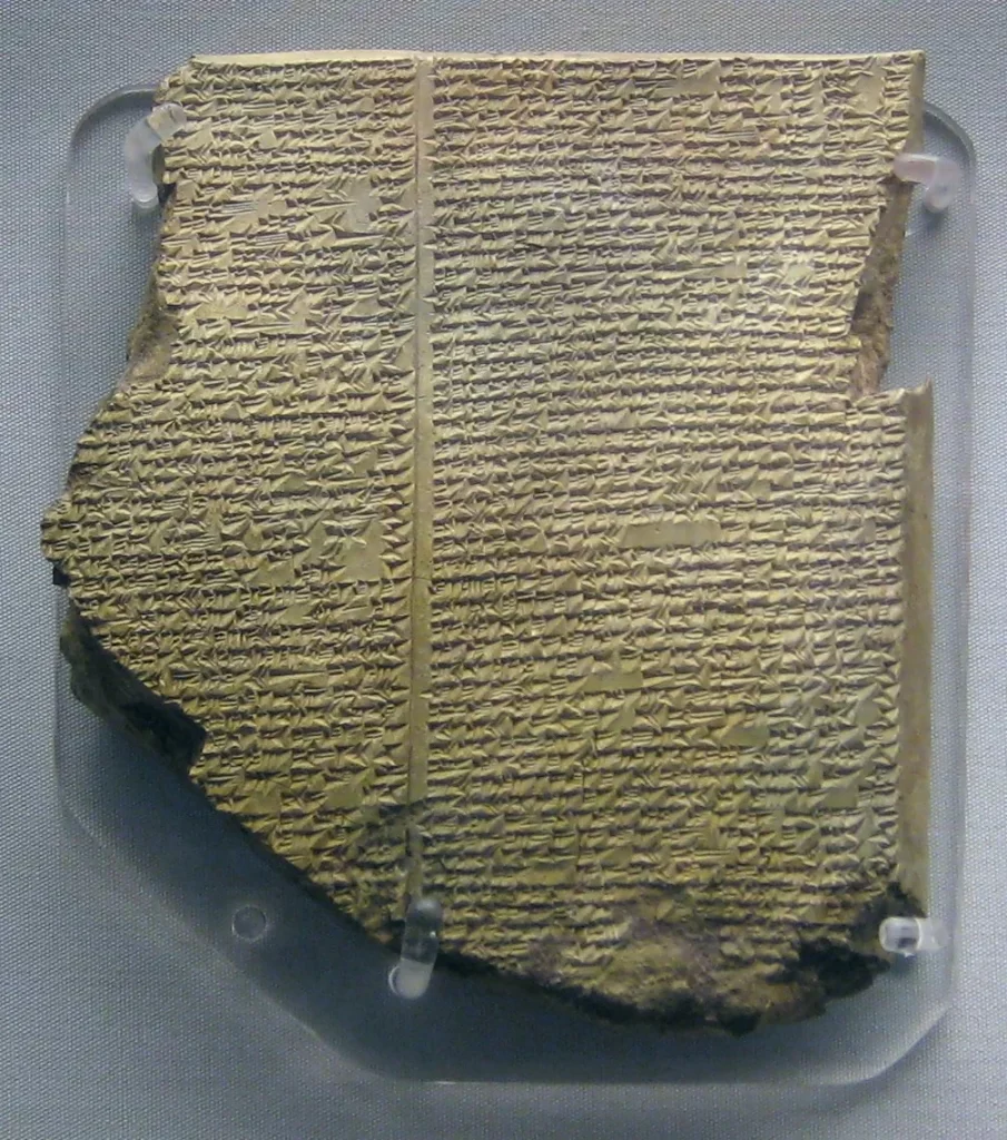 A broken tablet of pale brown clay covered with close lines of small wedge-shaped writing in two columns.